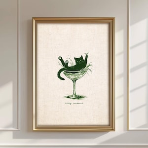 May include: A framed print featuring a green illustration of a black cat lounging in a cocktail glass. The cat is surrounded by splashes, with the words "kitty cocktail" written below. The frame is gold.