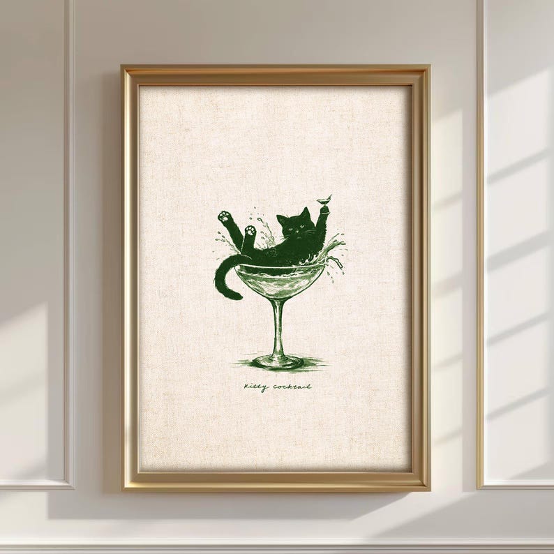 May include: A framed print featuring a green illustration of a black cat lounging in a cocktail glass. The cat is surrounded by splashes, with the words "kitty cocktail" written below. The frame is gold.