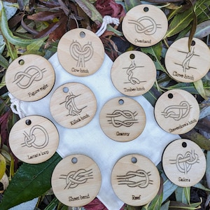 May include: A set of 12 wooden circles with different knots tied on them. Each circle has a hole at the top and a label with the name of the knot. The knots include: Figure eight, Lariat's loop, Cow hitch, Overhand, Timber hitch, Killick hitch, Clove hitch, Granny, Steveedore's hitch, Sheet bend, Reef, and Sailor's.