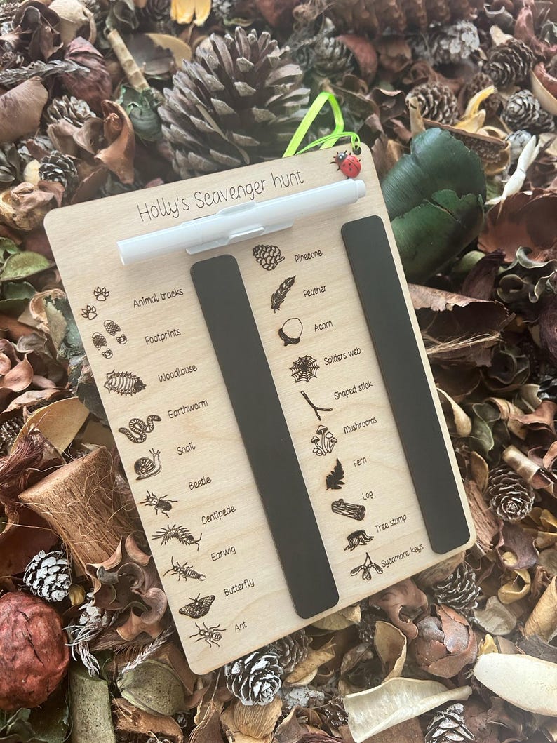 A wooden scavenger hunt board with various animal and plant illustrations, placed on a bed of pine needles and leaves.