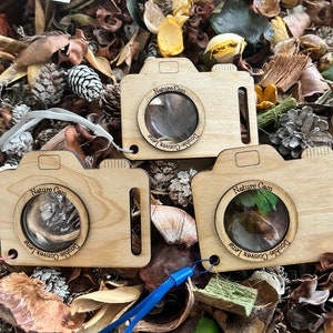 Puede incluir: Tres lupas de madera con forma de cámara con el texto "Nature Cam" y "Double-Convex Lens" impreso en ellas. Las lupas están sobre un lecho de hojas secas y otros materiales naturales.