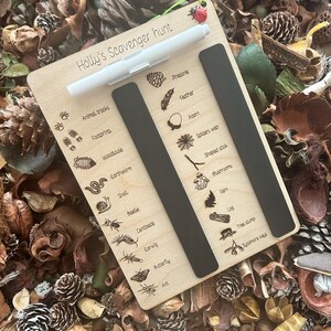 A wooden scavenger hunt board with various animal and plant illustrations, surrounded by pine cones, leaves, and other natural elements.