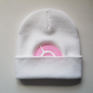 Può includere: Berretto di lana bianco con un logo circolare rosa.