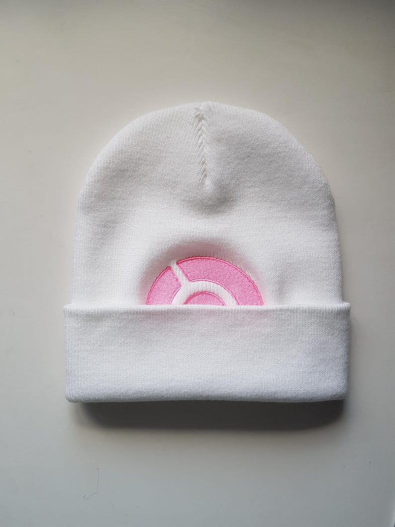 Puede incluir: Gorro de punto blanco con un logotipo circular rosa.