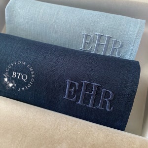 May include: Three linen handkerchiefs in a box. The top handkerchief is light blue, the middle handkerchief is dark blue, and the bottom handkerchief is beige. All three handkerchiefs have the initials "EHR" embroidered in white thread.