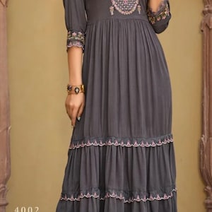 May include: A gray tiered dress with embroidered details and a round neckline. The dress has a ruffled hem and is worn with clear heeled sandals.