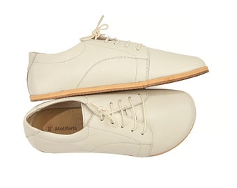 May include: A pair of off-white leather lace-up shoes with a brown sole. The shoes are stacked on top of each other.