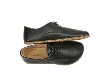 May include: A pair of black leather lace-up shoes with a brown stitched sole. The shoes are stacked on top of each other.