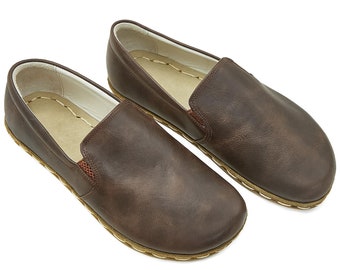 May include: A pair of brown leather slip-on shoes. The shoes have a rounded toe, a stitched sole, and a light-colored interior. The leather has a slightly distressed appearance. The shoes are designed for comfort and casual wear.