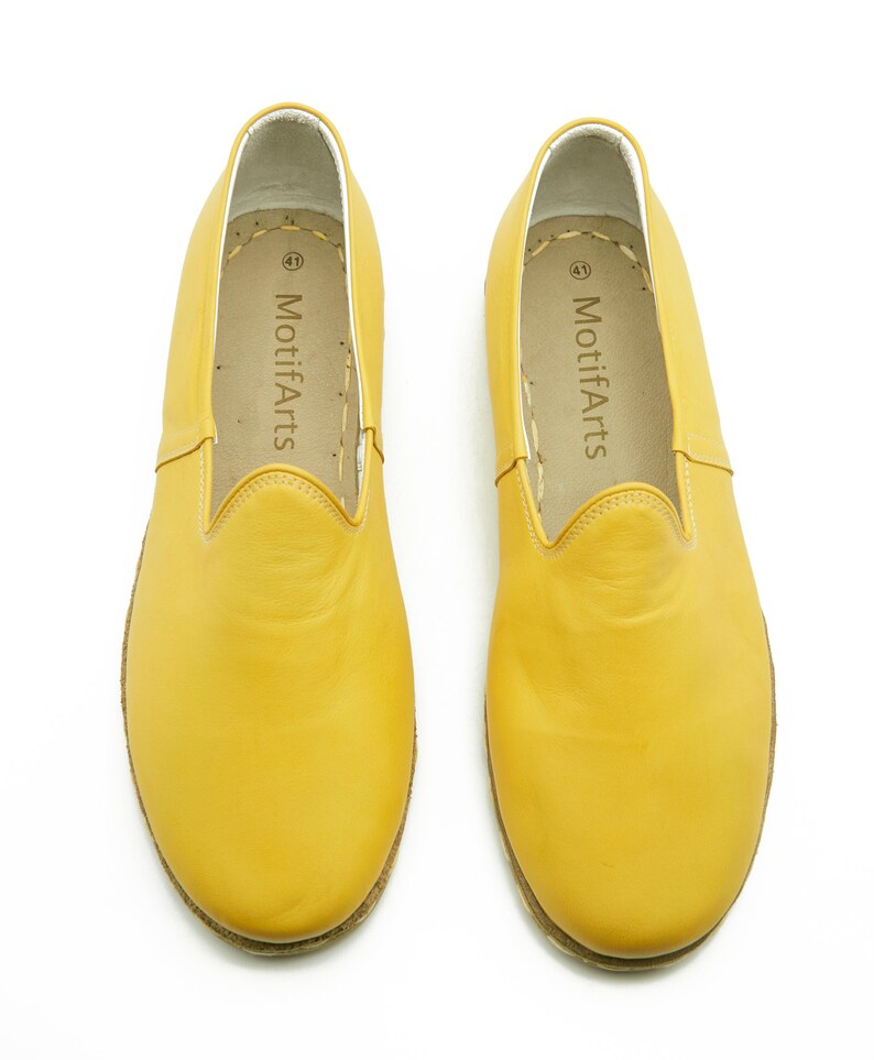 Puede incluir: Un par de zapatos de cuero amarillo de vestir sin cordones con el nombre de la marca "MotifArts" impreso en el interior de cada zapato.