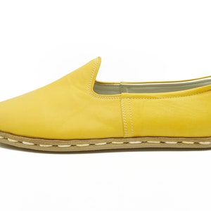 Puede incluir: Un par de zapatos amarillos de cuero con un detalle de costura blanca alrededor de la suela.