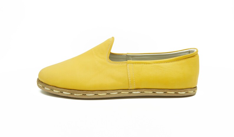 Puede incluir: Un par de zapatos amarillos de cuero con un detalle de costura blanca alrededor de la suela.