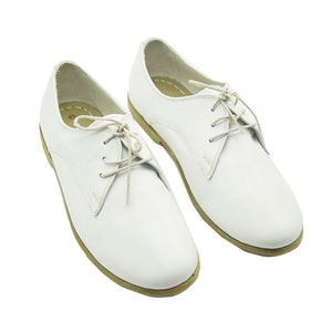 Puede incluir: Un par de zapatos blancos de cuero con cordones y suela de color crema.