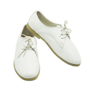 Puede incluir: Un par de zapatos blancos de cuero con cordones y tac&oacute;n bajo.