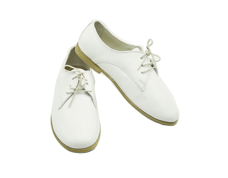 Puede incluir: Un par de zapatos blancos de cuero con cordones y tac&oacute;n bajo.