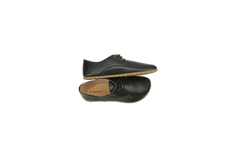 May include: A pair of black leather lace-up shoes with a brown stitched edge. The shoes are stacked on top of each other.