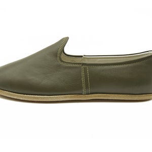 K&ouml;nnte beinhalten: Ein Paar olivgr&uuml;ne Lederschuhe zum Reinschl&uuml;pfen mit schlichtem Design und hellbrauner Sohle.