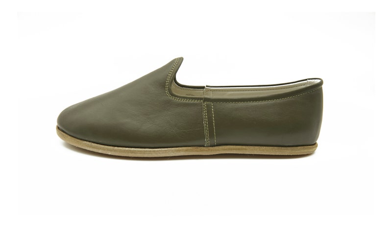 K&ouml;nnte beinhalten: Ein Paar olivgr&uuml;ne Lederschuhe zum Reinschl&uuml;pfen mit schlichtem Design und hellbrauner Sohle.