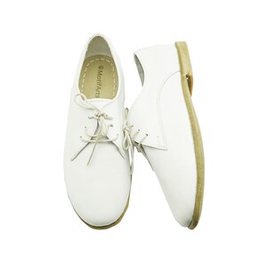 Puede incluir: Un par de zapatos blancos de cuero con cordones y suela marr&oacute;n. Los zapatos tienen un dise&ntilde;o sencillo y est&aacute;n hechos de un material suave y c&oacute;modo. El nombre de la marca "MotifArts" est&aacute; impreso en el interior del zapato.
