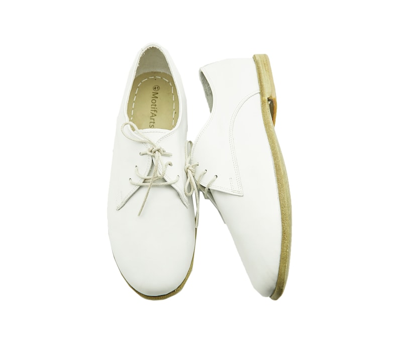 Puede incluir: Un par de zapatos blancos de cuero con cordones y suela marr&oacute;n. Los zapatos tienen un dise&ntilde;o sencillo y est&aacute;n hechos de un material suave y c&oacute;modo. El nombre de la marca "MotifArts" est&aacute; impreso en el interior del zapato.