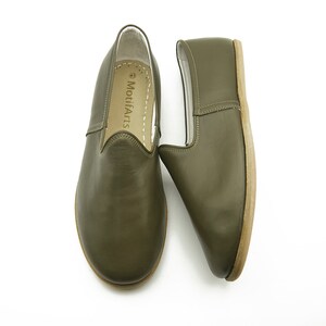 K&ouml;nnte beinhalten: Ein Paar olivgr&uuml;ne Slipper aus Leder mit wei&szlig;em Lederfutter. Die Schuhe haben ein schlichtes Design und sind aus weichem, geschmeidigem Leder gefertigt. Der Markenname "MotifArts" ist auf der Innenseite des Schuhs aufgedruckt.