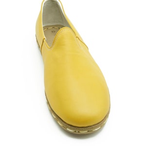 Puede incluir: Un par de zapatos amarillos de cuero con un ribete blanco cosido alrededor de la suela.