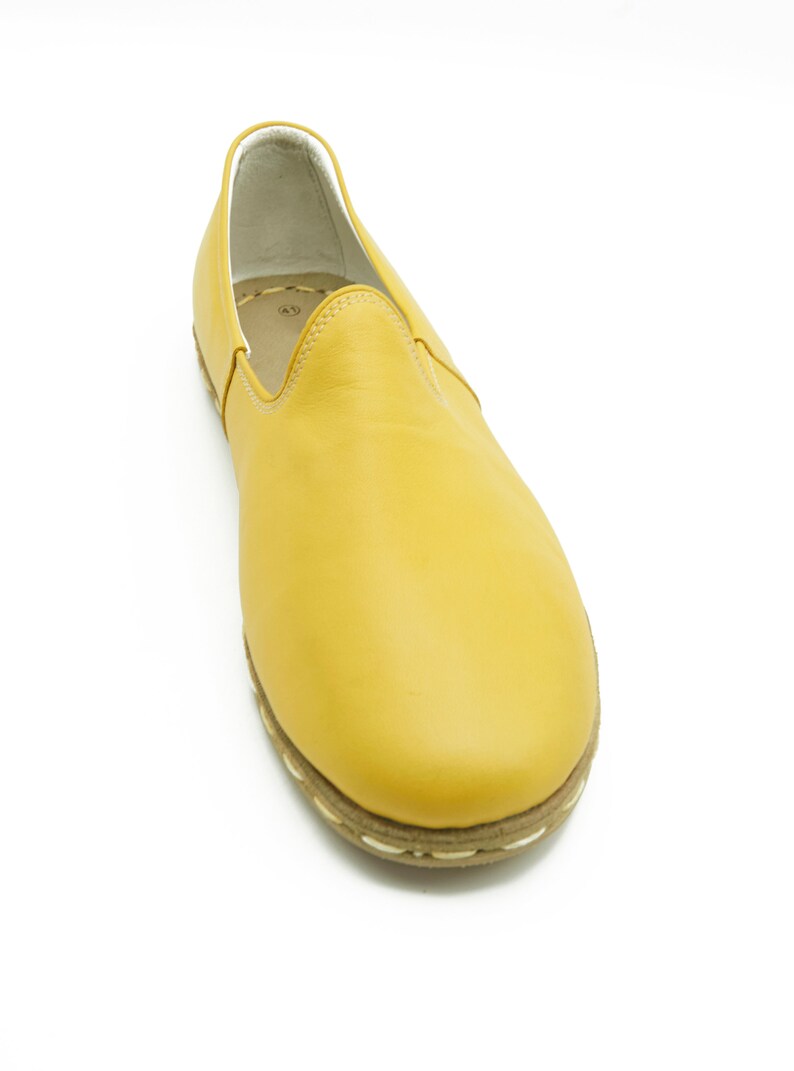Puede incluir: Un par de zapatos amarillos de cuero con un ribete blanco cosido alrededor de la suela.