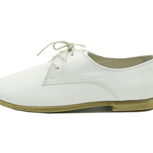 Puede incluir: Zapatos blancos de cuero con cordones y suela marr&oacute;n.
