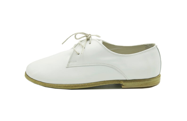 Puede incluir: Zapatos blancos de cuero con cordones y suela marr&oacute;n.
