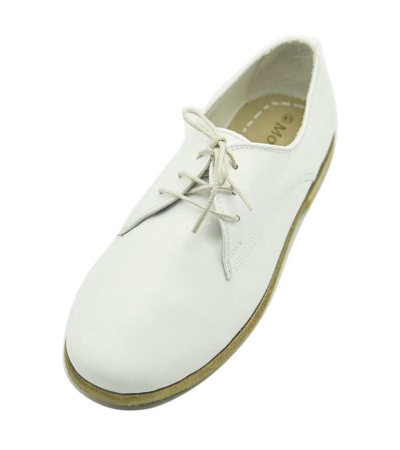 Puede incluir: Zapatos de cuero blanco con cordones y suela marr&oacute;n. Los zapatos tienen un dise&ntilde;o sencillo y est&aacute;n hechos de cuero de alta calidad.