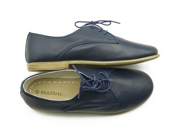 May include: A pair of navy blue leather lace-up shoes with a brown sole. The shoes have a simple design and are made of high-quality leather. The inside of one shoe has the text "MotifArts" printed on the insole.