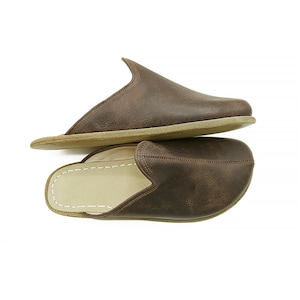 May include: A pair of brown leather slippers with a closed toe and a slip-on design. The slippers have a suede sole and a soft, comfortable lining.