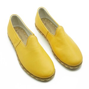 Puede incluir: Un par de zapatos amarillos de cuero con un borde cosido y el nombre de la marca "MotifArts" en el interior de cada zapato.