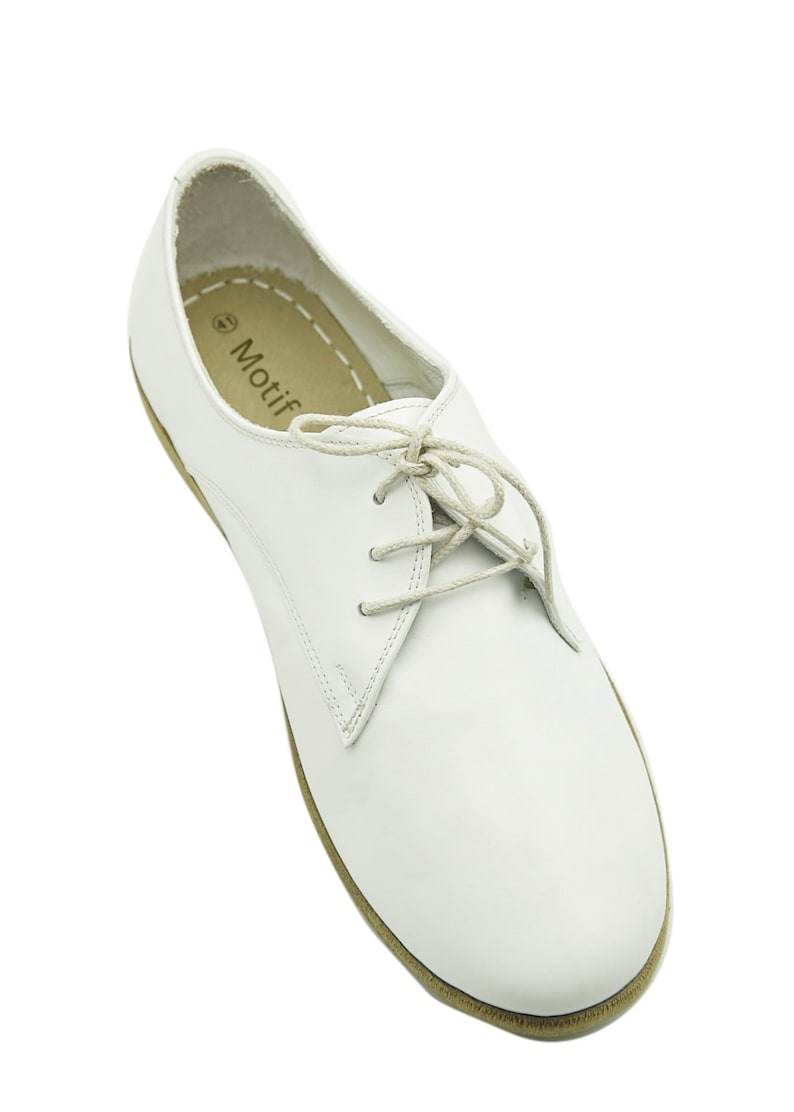 Puede incluir: Zapatos blancos de cuero con cordones y suela marr&oacute;n. Los zapatos tienen un dise&ntilde;o sencillo y est&aacute;n hechos de un material suave y c&oacute;modo. El nombre de la marca "Motif" est&aacute; impreso en la plantilla.