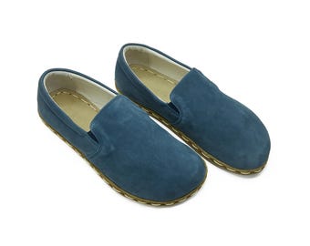 May include: A pair of blue suede slip-on shoes with a brown rubber sole.