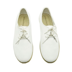 Puede incluir: Un par de zapatos de cuero blanco con cordones y suela marr&oacute;n. Los zapatos tienen el texto "MotifArts" impreso en el interior de cada zapato.