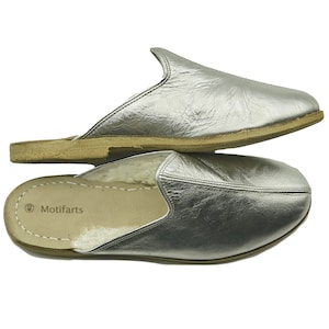 May include: A pair of silver leather slippers with a brown suede sole. The slippers have a fluffy white lining and the brand name "Motifarts" is printed on the insole.