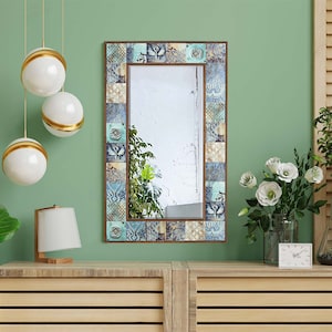 May include: A rectangular mirror with a decorative frame made of blue, green, and brown tiles. The mirror is hanging on a green wall above a wooden dresser.