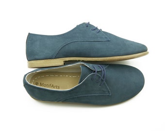 May include: A pair of blue suede lace-up shoes with a brown sole. The shoes are stacked on top of each other. The brand name "MotifArts" is visible on the inside of the shoe.