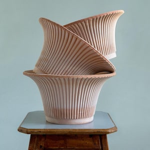 Könnte beinhalten: Drei gestapelte Blumentöpfe aus Terrakotta mit geriffeltem Design. Die Töpfe haben einen breiten, gezahnten Rand und eine hellbraune Farbe. Sie stehen auf einem kleinen Holztisch mit einer blau-grauen Oberfläche.