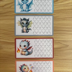 May include: Four rectangular reward charts featuring illustrations of baby dragons. Each chart displays a unique dragon character on the left and a grid of sixteen empty flame-shaped outlines on the right for tracking progress or goals.