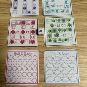 May include: A selection of game boards with different themes, such as dice, trees, and clouds. Each board has a grid for tracking progress, with some labeled "Roll & Save". A die showing the number 25 is also included. Measurements are in cm.