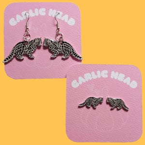May include: Two pairs of earrings with a spotted leopard design. One pair are drop earrings, and the other are stud earrings. The earrings are presented on pink cards with the text "GARLIC HEAD" in white.
