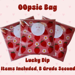 May include: Three clear plastic bags containing items, each featuring a repeating pattern of red strawberries and white flowers with yellow centers on a pink background. Each bag has a circular white label with two small pink hearts and text.