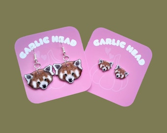 Puede incluir: Un par de pendientes de panda rojo y un juego de pendientes de panda rojo en tarjetas rosas con el texto "GARLIC HEAD".