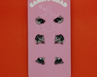 May include: A pink card with the text "Garlic Head" printed in white. The card features four pairs of black and white rat earrings.