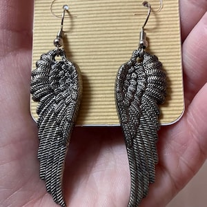 May include: A pair of silver angel wing earrings with a detailed feather design.