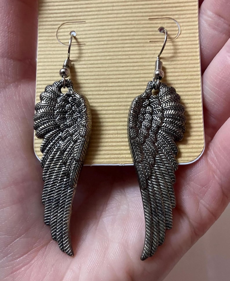 May include: A pair of silver angel wing earrings with a detailed feather design.