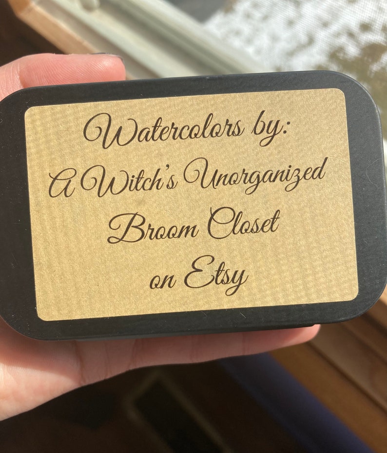K&ouml;nnte beinhalten: Eine schwarze Dose mit einem braunen Papieretikett, auf dem "Watercolors by: A Witch's Unorganized Broom Closet on Etsy" steht.