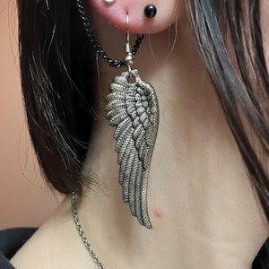 May include: A silver wing-shaped earring with a chain attached to a black hoop earring. The earring is worn in the earlobe and the hoop is worn in the upper ear.